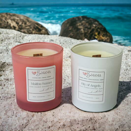 two candles one in a pink jar and one in a white jar sitting in the sand with water in the background